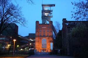 4348518862_4aafb7430c_h(1).jpg: Backsteinbau des Malakoffturms mit beleuchtetem Fördergerüst der Zeche Prosper in der Abenddämmerung