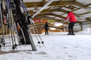 Alpincenter, Bottrop: Langlaufstrecke in einer Halle mit Skiern im Vordergrund und Menschen beim Training.