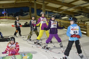 alpincenter, Bottrop: Kinder mit Helmen und Skiern üben in der Skihalle des alpincenters Bottrop auf einer Schneepiste.