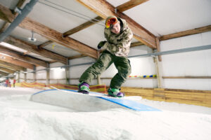 alpincenter, Bottrop: Snowboarder springt in der Skihalle Bottrop über eine Rampe auf schneebedeckter Indoorpiste.