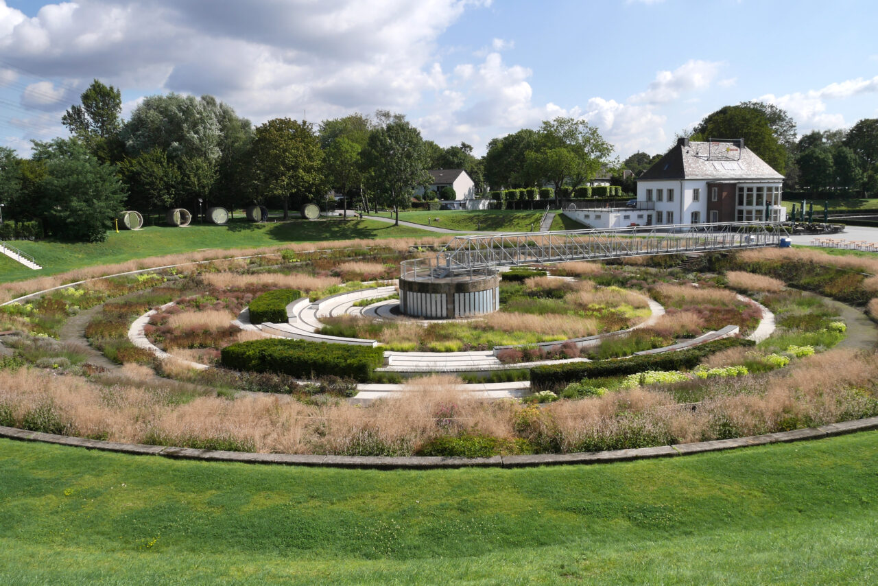 BernePark, Bottrop: Rundbecken im BernePark Bottrop mit üppiger Bepflanzung, Stegen und angrenzendem Betriebsgebäude.