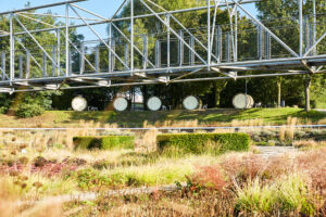 Bernepark Bottrop: Eine moderne Brückenkonstruktion überquert einen gepflegten Park mit geometrischen Hecken und Gräsern.