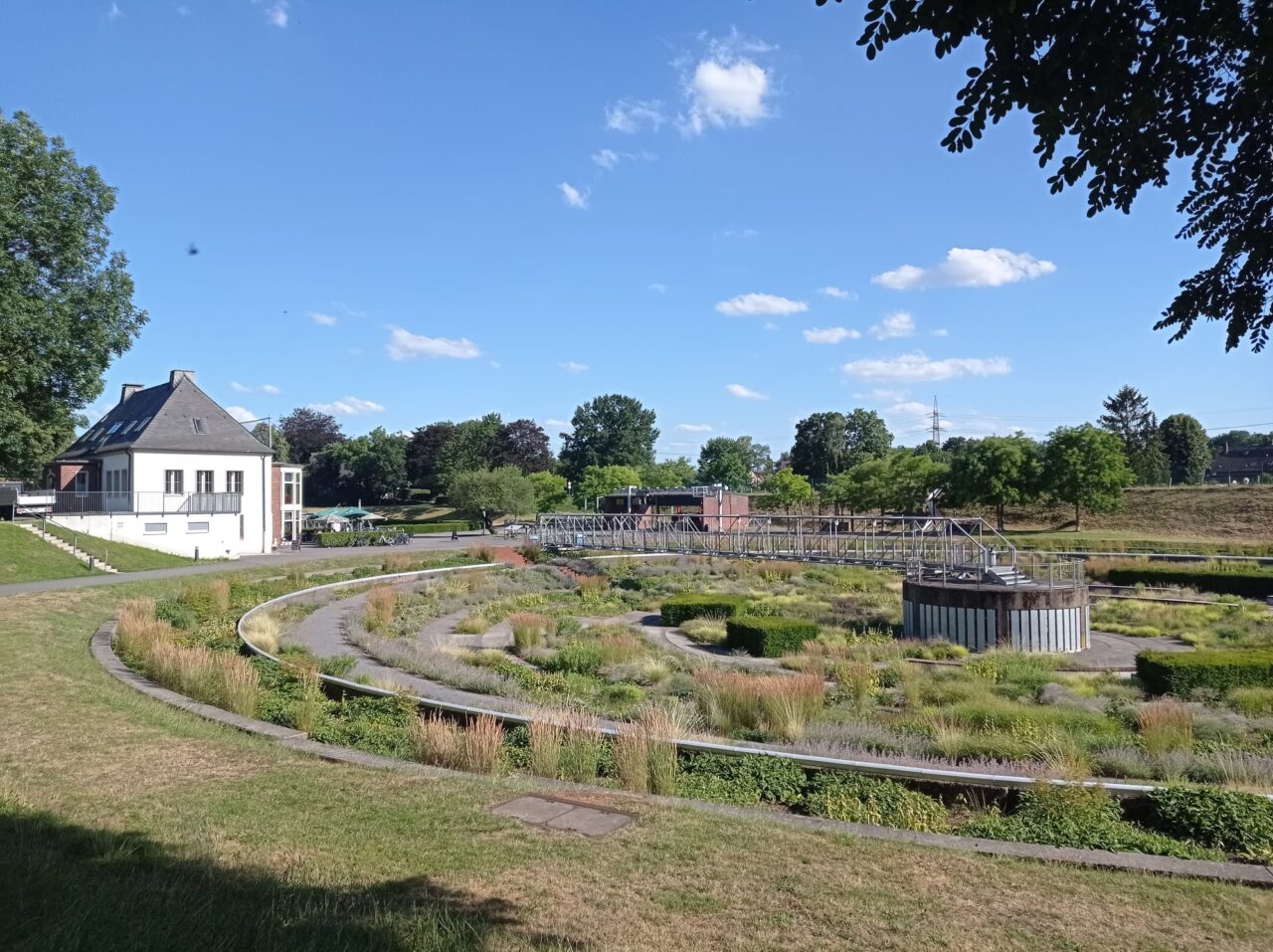 BernePark, Bottrop: Grüne Parklandschaft mit bepflanzten Becken, Fußwegen und Gebäuden im BernePark Bottrop bei Sonne
