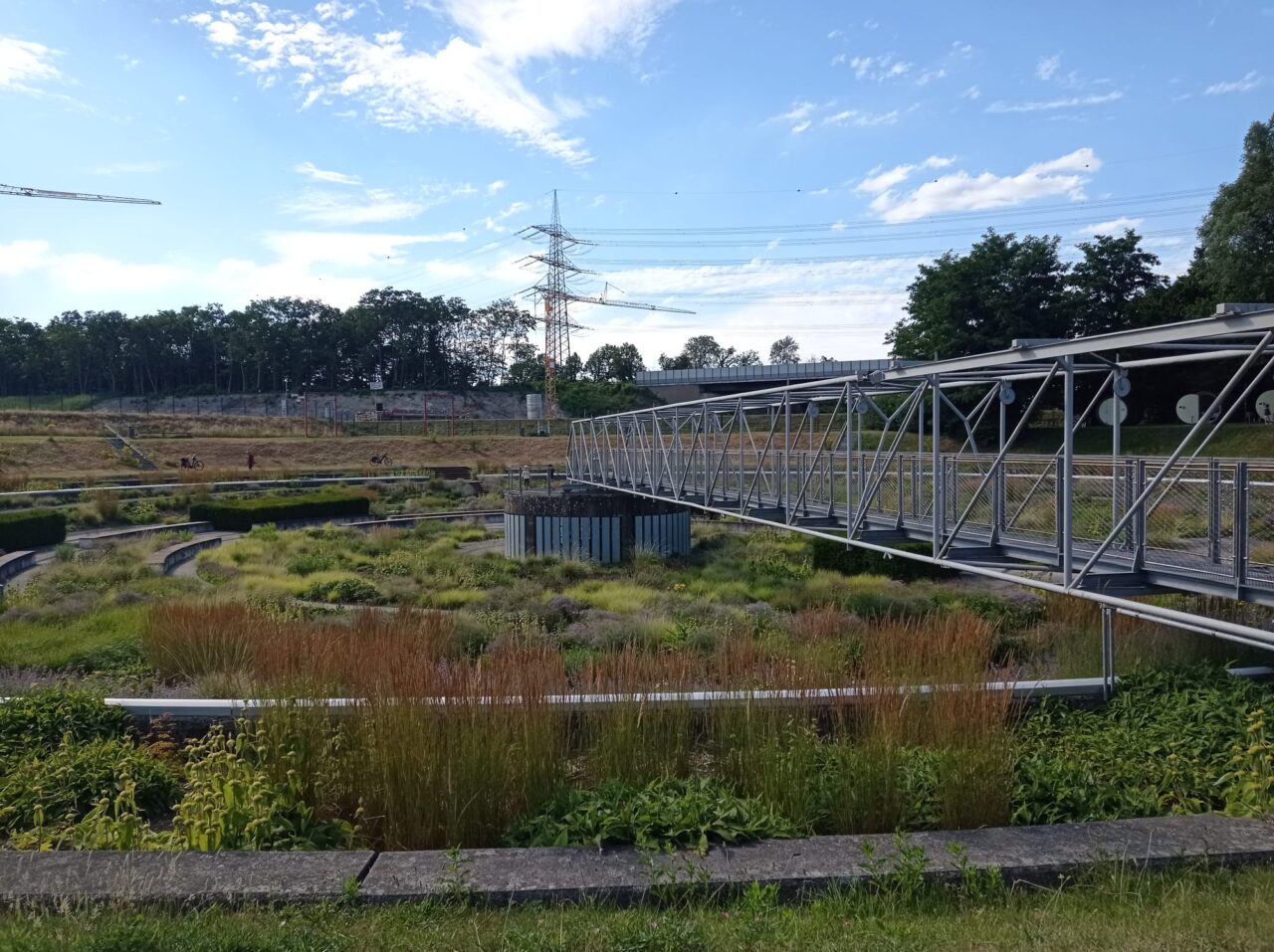 BernePark, Bottrop: Metallsteg über bepflanzte Becken im BernePark Bottrop unter blauem Himmel mit Wolken.