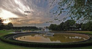 BernePark, Bottrop, Becken: Rundes Becken im BernePark Bottrop, umgeben von Grünflächen und Bäumen bei Abendlicht.