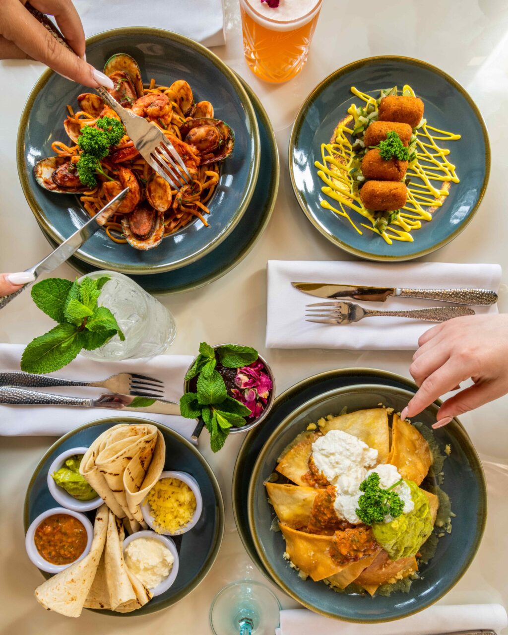 bottrop+bodega-tapas-bar+bild02.jpg: Vier Teller auf einem Tisch, gefüllt mit spanischen Tapas und Getränken, werden mit Gabeln erkundet.