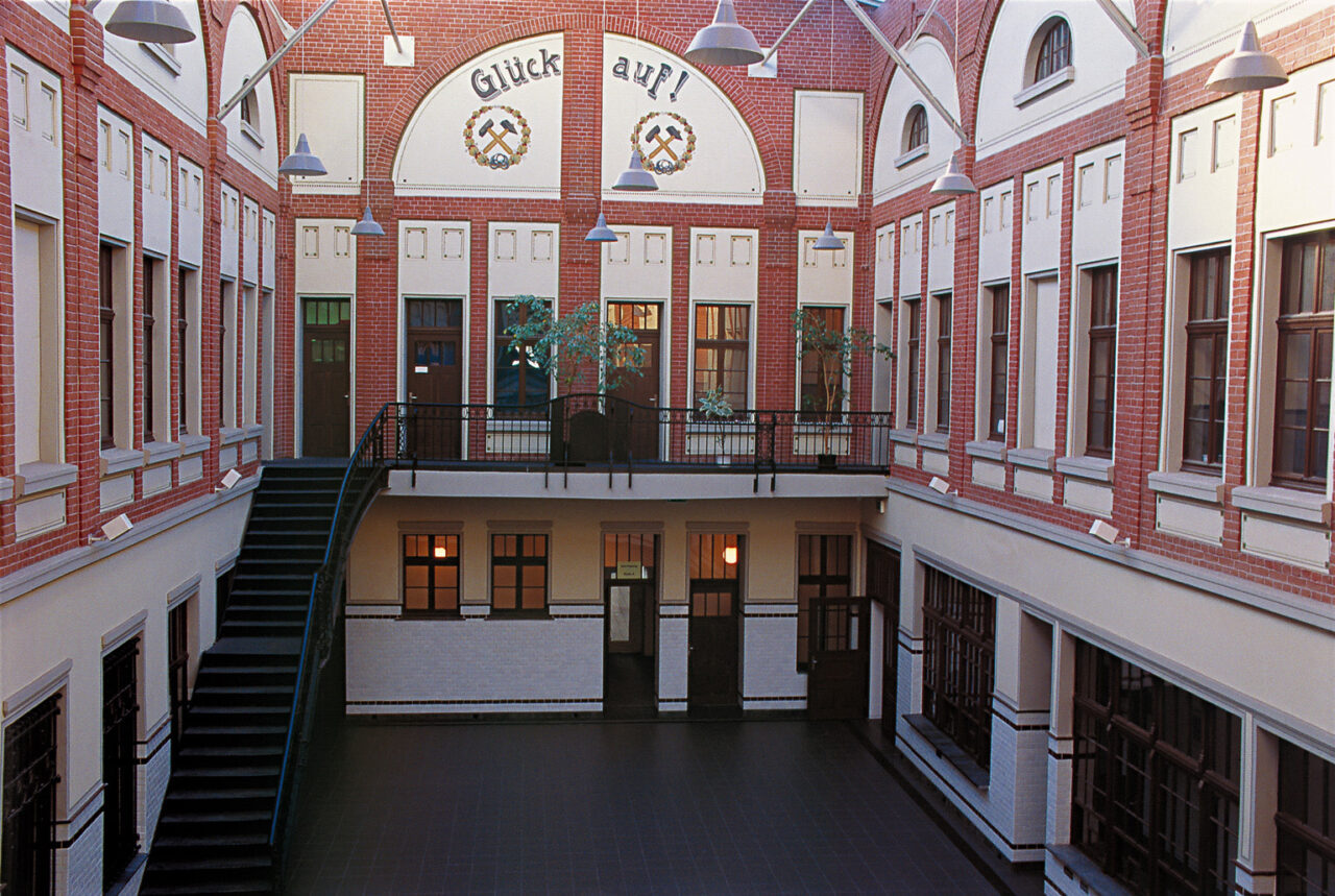 Bottrop Lohnhalle.jpg: Innenhof der Lohnhalle Bottrop mit Backsteinfassade, Empore, Treppe und Schriftzug „Glück auf!“