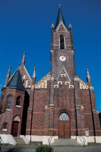 Bottrop_Martinskirche.jpg: Backsteinkirche mit hohem Turm, spitzem Dach und Uhrzifferblatt vor klarem, blauem Himmel.