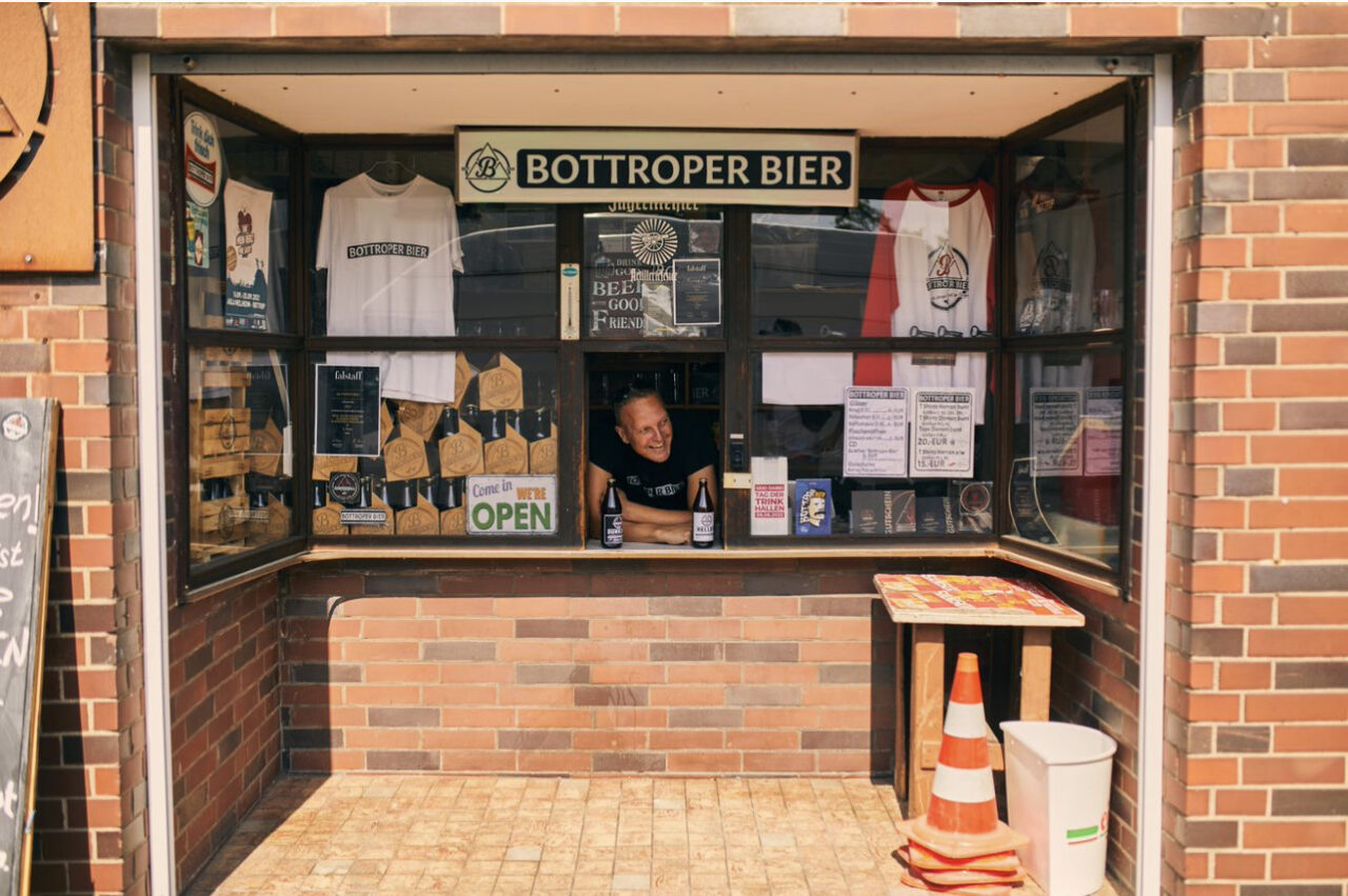 Bottroper Bier, Bottrop: ```html
Verkaufskiosk aus Backsteinen in Bottrop, beschildert mit "Bottroper Bier". Ein Mann bedient.
```
