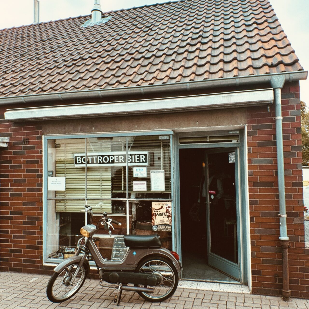 Bottroper Bier, Bottrop: Ein kleines Backsteingebäude mit einem Schild "Bottroper Bier" daneben ein altes Motorrad.