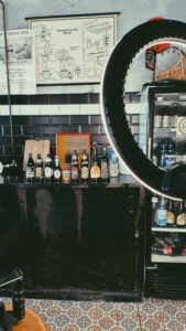 Bottroper Bier, Bottrop: Blick in eine gemütliche Bar mit verschiedenen Bierflaschen auf einer Theke und einem Regal im Hintergrund.