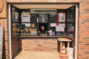 Bottroper Bier, Bottrop: ```html
Verkaufskiosk aus Backsteinen in Bottrop, beschildert mit "Bottroper Bier". Ein Mann bedient.
```