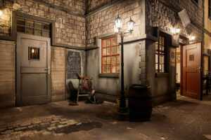 ELORIA Erlebnisfabrik Bottrop: Historische Straßenszene mit Laternenlicht beleuchtet. Pony-Sattel auf Barhocker vor Steinmauer.