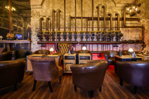 ELORIA Erlebnisfabrik Bottrop: Eine industriell gestaltete Bar mit Ledersesseln und alten Rohrleitungen an der Wand.