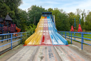 Freizeitpark Schloss Beck Bottrop: ```html
Große, bunte Rutsche mit fünf Bahnen in einem Park, umgeben von Bäumen und Spielgeräten.
```