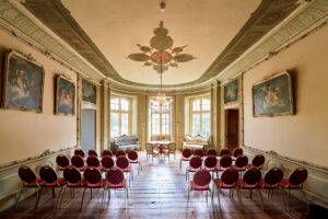 Freizeitpark Schloss Beck Bottrop: Historischer Saal mit antiken Gemälden, Kronleuchter und bestuhltem Publikum auf Parkettboden.