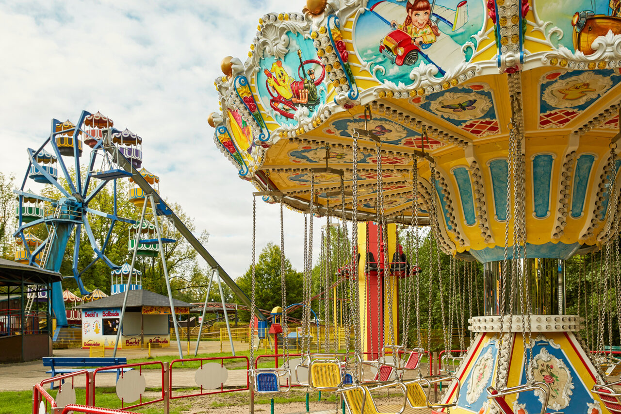 Freizeitpark Schloss Beck Bottrop: Ein bunter Karussellplatz mit einem Kettenkarussell und Riesenrad bei strahlendem Sonnenschein.