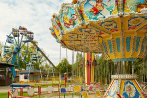 Freizeitpark Schloss Beck Bottrop: Ein bunter Karussellplatz mit einem Kettenkarussell und Riesenrad bei strahlendem Sonnenschein.