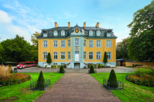 Freizeitpark Schloss Beck, Bottrop: Gelbes Barockschloss mit symmetrischer Fassade, Gartenweg und roter Parkbahn im Vordergrund