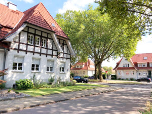 Gartenstadt Welheim, Bottrop: Straßenszene mit historischen Siedlungshäusern der Gartenstadt Welheim unter alten, grünen Bäumen.