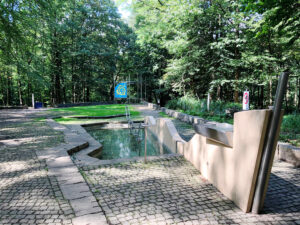 Gesundheitspark Quellenbusch, Bottrop: Flacher Kneippbeckenbereich im Gesundheitspark Quellenbusch, umgeben von Bäumen und Pflastersteinen.
