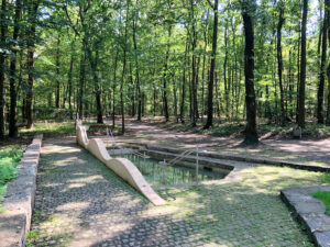 Gesundheitspark Quellenbusch, Bottrop, Wald: Kneippbecken im schattigen Wald des Gesundheitsparks Quellenbusch mit hellem Steinrand und Bäumen.