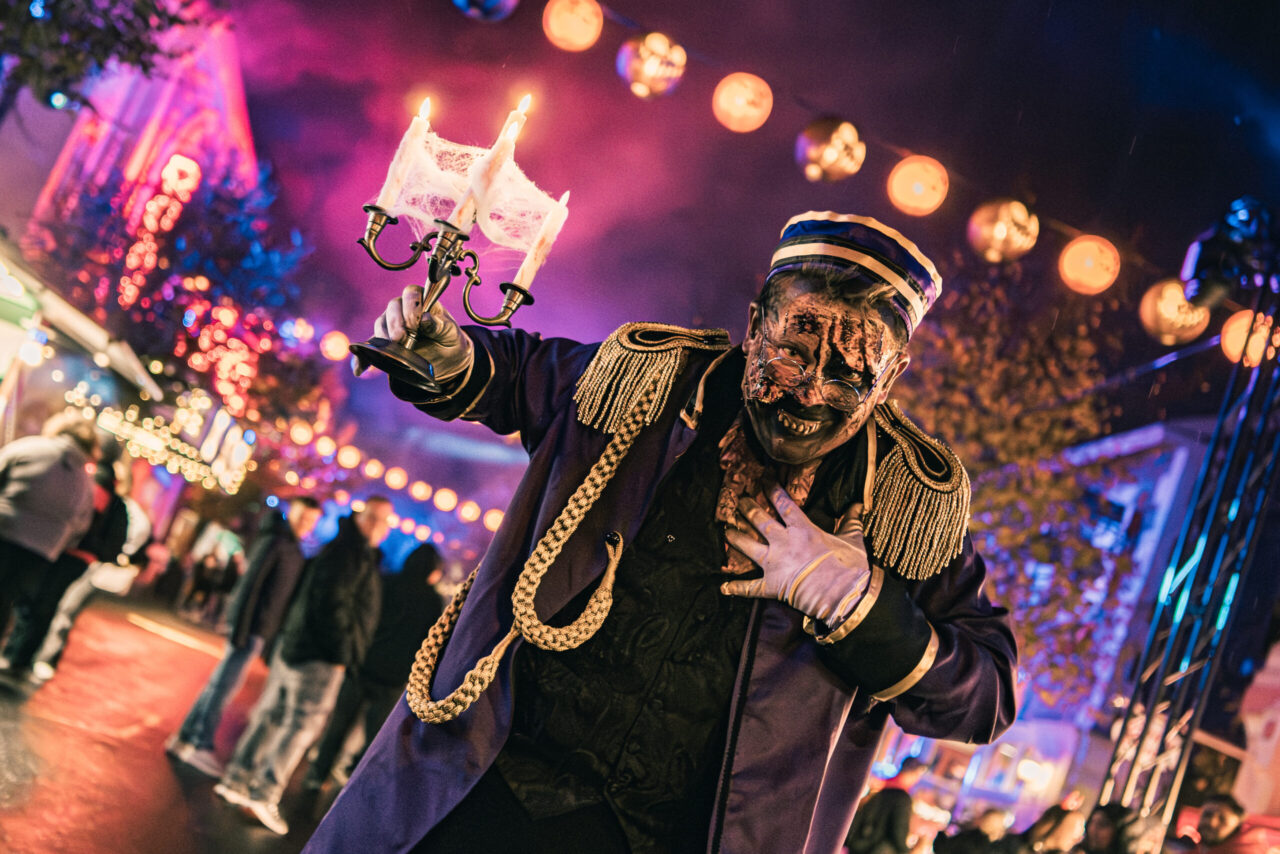 Halloween Horror Festival, Movie Park Germany: Gruselige Gestalt in Uniform mit Kerzenleuchter auf beleuchtetem Nachtfest.