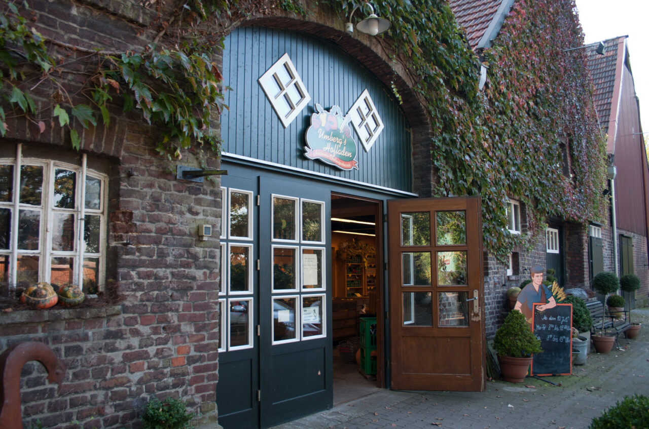 Hof Umberg, Bottrop: Eingang eines Hofladens in einem Backsteingebäude mit Efeubewuchs und offenen Holztüren.