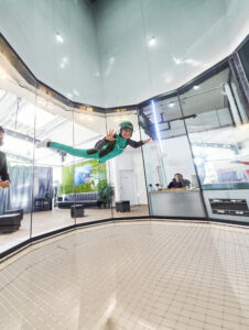 Indoor Skydiving, Bottrop, Flug: Person mit Schutzhelm und Anzug schwebt in einer vertikalen Windröhre beim Indoor Skydiving in Bottrop.