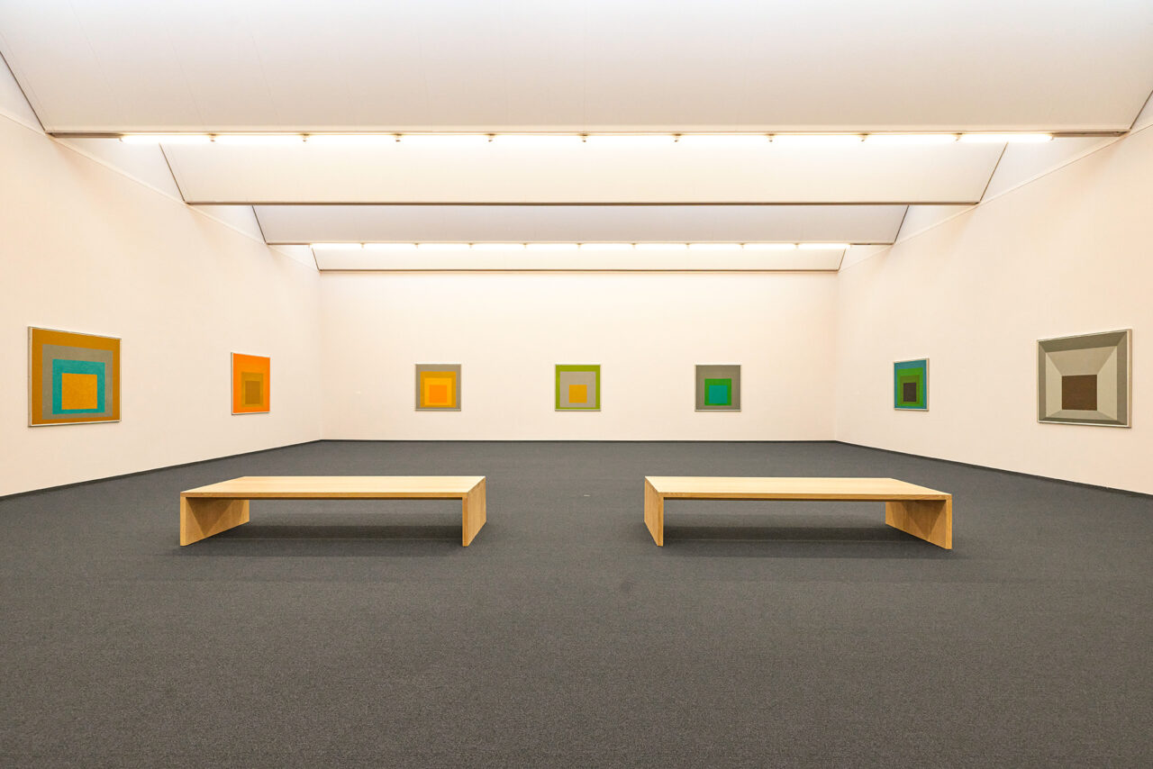Josef Albers Museum Quadrat, Bottrop: Zwei Holzbanken in einem modernen, minimalistischen Museumsraum mit kunterbunten quadratischen Bildern an den cremefarbenen Wänden.