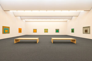 Josef Albers Museum Quadrat, Bottrop: Zwei Holzbanken in einem modernen, minimalistischen Museumsraum mit kunterbunten quadratischen Bildern an den cremefarbenen Wänden.