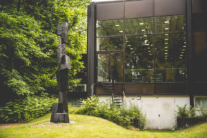 Josef Albers Museum Quadrat Bottrop: Großes gläsernes Museumsgebäude im Grünen mit schwarzer abstrakter Skulptur im Vordergrund