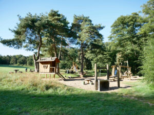 Kirchheller Heide, Bottrop, Waldspielplatz: Holzspielplatz im Wald mit Rutsche, Klettergeräten und Wiesenfläche unter hohen grünen Bäumen
