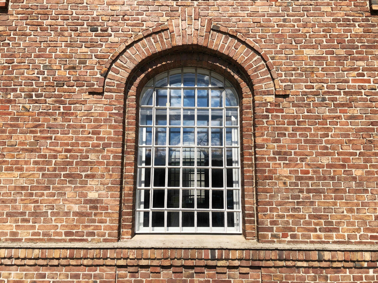 Lokschuppen, Bottrop, Nahaufnahme Fenster: Großes Rundbogenfenster mit Gitterstruktur in einer Fassade aus rötlich-braunem Backsteinmauerwerk.
