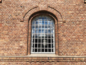 Lokschuppen, Bottrop, Nahaufnahme Fenster: Großes Rundbogenfenster mit Gitterstruktur in einer Fassade aus rötlich-braunem Backsteinmauerwerk.
