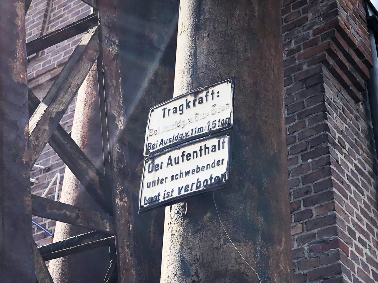 Lokschuppen, Bottrop, Nahaufnahme, innen: Rostige Stahlträger und ein Hinweisschild zur Tragkraft im Innern des Lokschuppens Bottrop