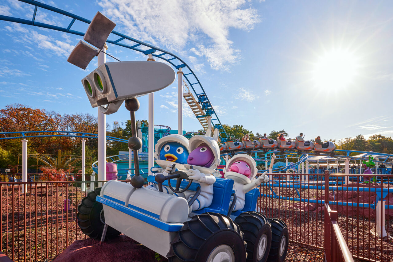 Movie Park Germany Bottrop: Comic-Figuren in Raumanzügen fahren ein Weltraumfahrzeug im Vergnügungspark unter blauem Himmel.