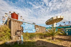 Movie Park Germany Bottrop: Alt-Text für das Bild: Freizeitpark mit Riesenrad, Kettenkarussell, Palmen und maritimem Dekor unter blauem Himmel.