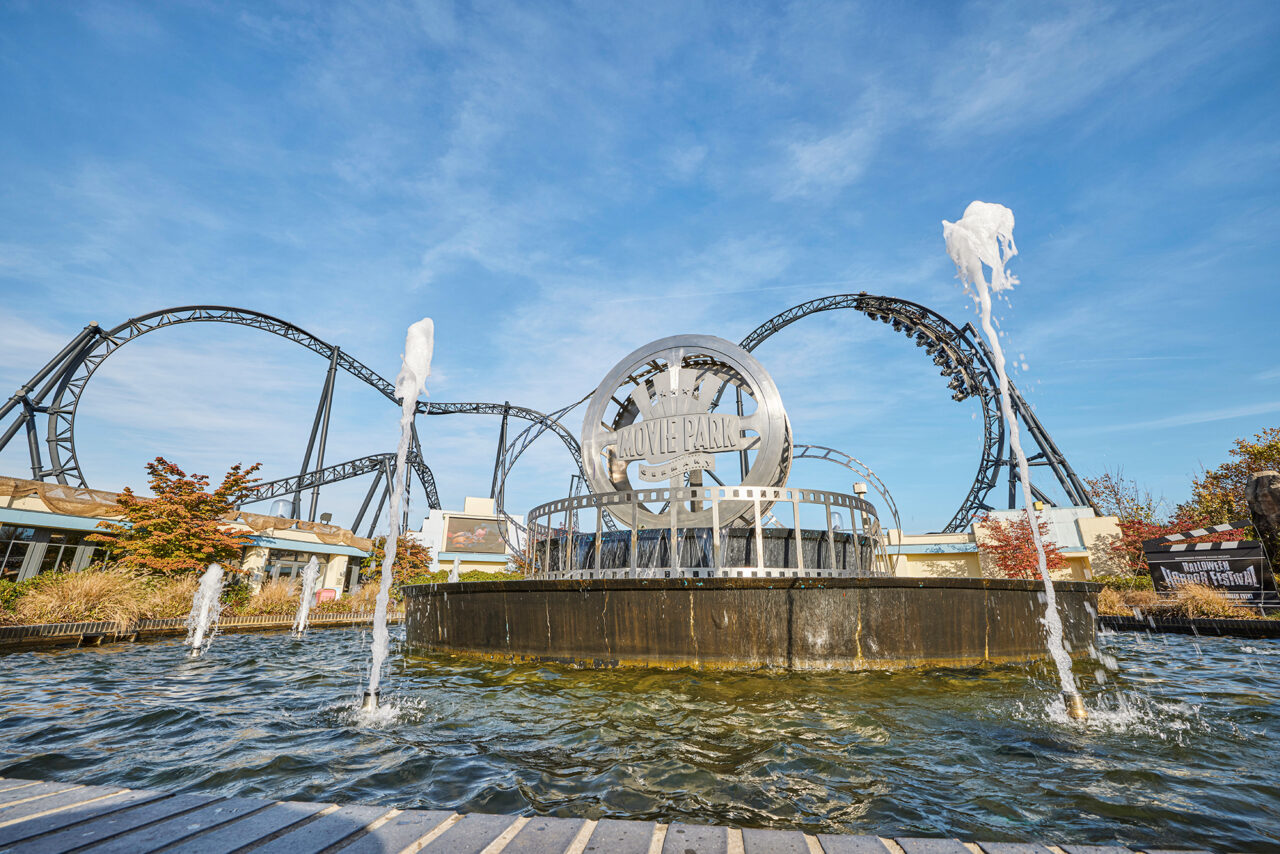 Movie Park Germany Bottrop: Filmparkemblem mit Achterbahn und Springbrunnen vor strahlend blauem Himmel in Bottrop.