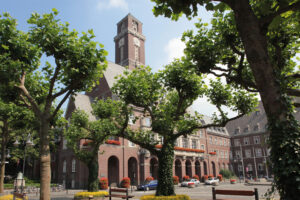 Rathaus, Bottrop, Blick zum Turm: Backsteinernes Rathaus Bottrop mit Uhrturm, begrüntem Vorplatz und blühenden Balkonkästen im Sommer.