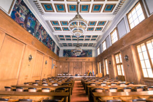 Rathaus, Bottrop, Sitzungssaal: Holzgetäfelter Sitzungssaal im Rathaus Bottrop mit Kronleuchtern, Wandgemälden und hohen Fenstern.