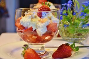 recklinghausen+eiscafe-il-gelato+bild01.jpg: Ein Glas mit Erdbeeren, Sahne und Mandelsplittern, dekoriert mit einer Erdbeere, steht auf einem Tisch.