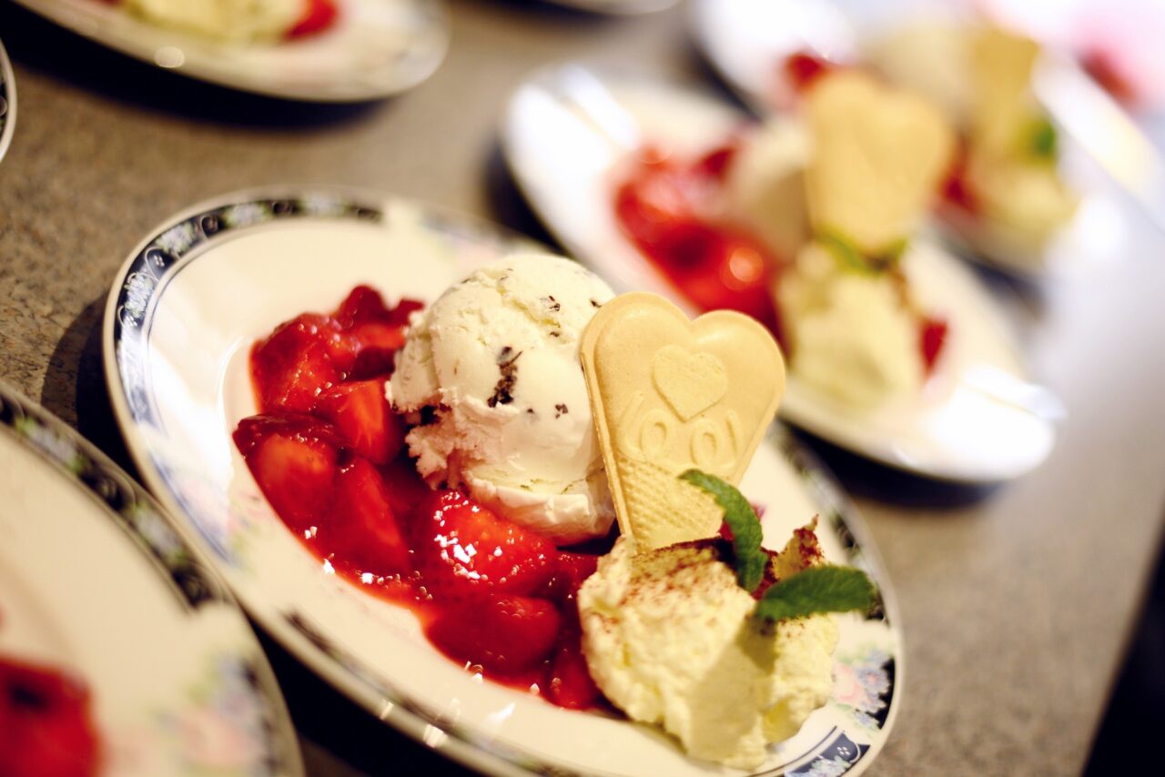 recklinghausen+eiscafe-il-gelato+bild03.jpg: Leckere Kugel Vanilleeis mit frischen Erdbeeren, Sahne, dekorativer Waffel und Minzblatt auf Teller.