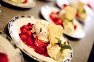 recklinghausen+eiscafe-il-gelato+bild03.jpg: Leckere Kugel Vanilleeis mit frischen Erdbeeren, Sahne, dekorativer Waffel und Minzblatt auf Teller.