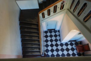 Schloß Beck, Bottrop: Holztreppe mit hellem Geländer und schwarz-weiß gefliestem Boden im Inneren von Schloss Beck.