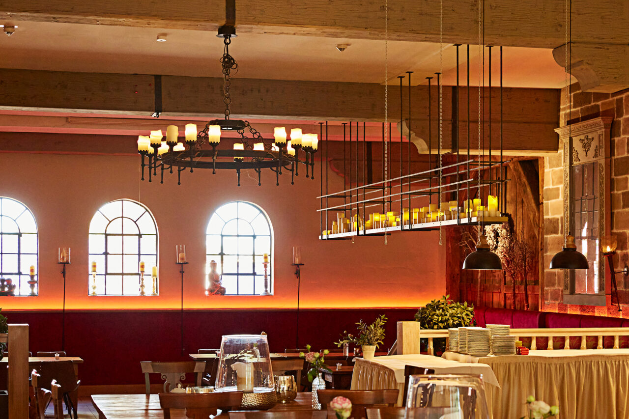 Schmücker Hof, Bottrop-Kirchhellen: Das Bild zeigt einen rustikalen, gemütlichen Gastraum mit Holztischen, Kerzenleuchtern und traditionellen Fenstern.