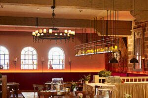 Schmücker Hof, Bottrop-Kirchhellen: Das Bild zeigt einen rustikalen, gemütlichen Gastraum mit Holztischen, Kerzenleuchtern und traditionellen Fenstern.