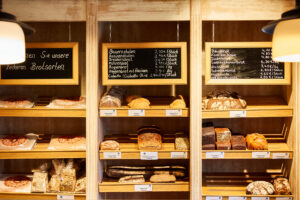 Schmücker Hof, Bottrop-Kirchhellen: Verschiedene Brotsorten und Gebäckstücke in einem Regal eines Bäckereigeschäfts, mit Preistafeln.