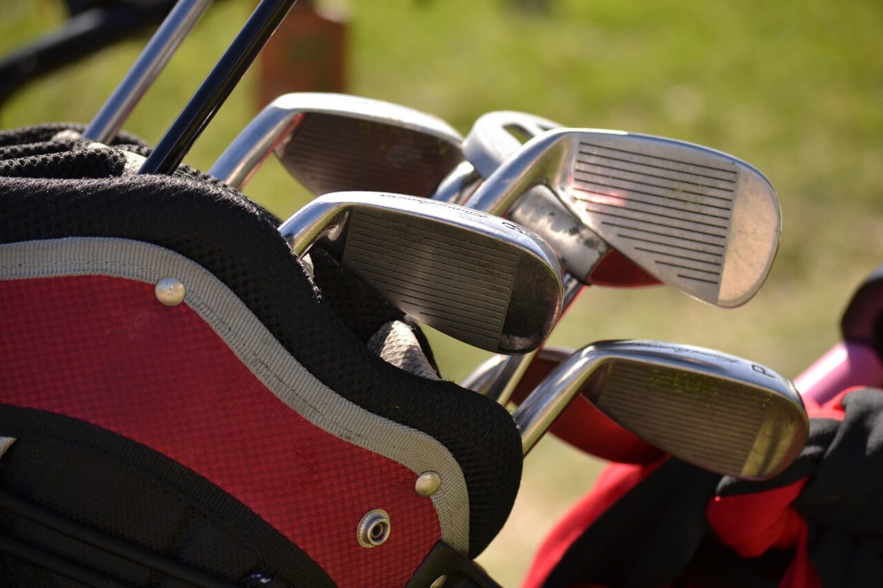 Stockfoto Golf: Golfschläger in einer rot-schwarzen Tasche vor unscharfem Hintergrund auf dem Gelände des Golfclubs.