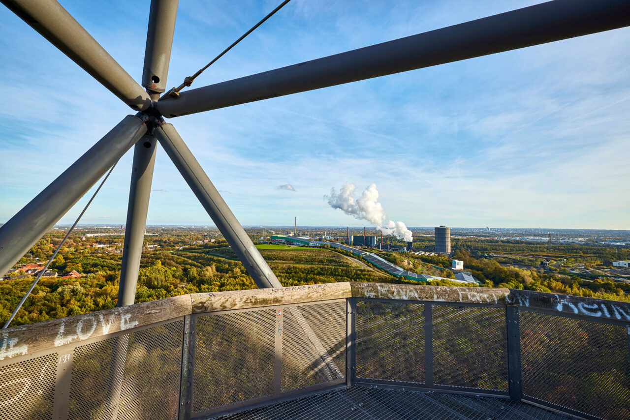 Tetraeder Halde Beckstr. Bottrop: Blick von Tetraeder Bottrop über das Ruhrgebiet, Schornsteine im Hintergrund, unter blauem Himmel.
